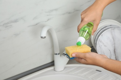 Photo of Woman pouring cleaning product for dish washing onto sponge near kitchen sink. Space for text