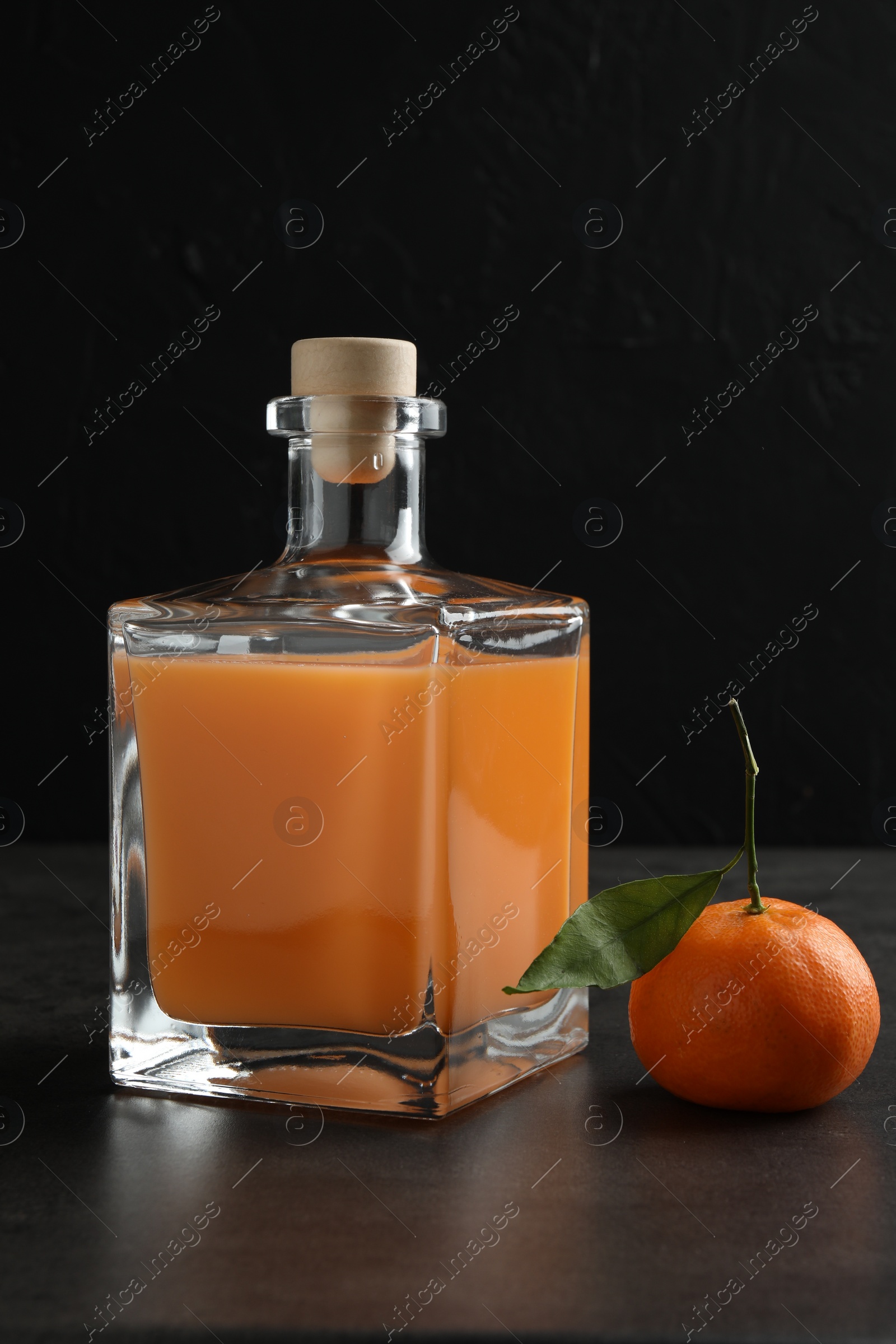Photo of Delicious tangerine liqueur in glass bottle and fresh fruit on grey table