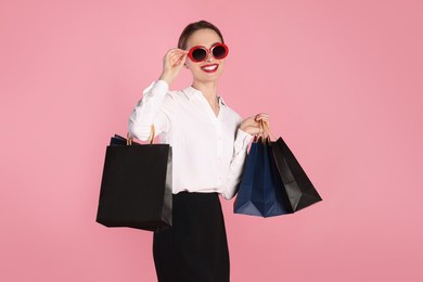 Photo of Happy young woman with shopping bags on light pink background. Big sale