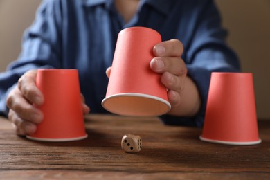 Photo of Woman playing thimblerig game with red cups at wooden table, closeup