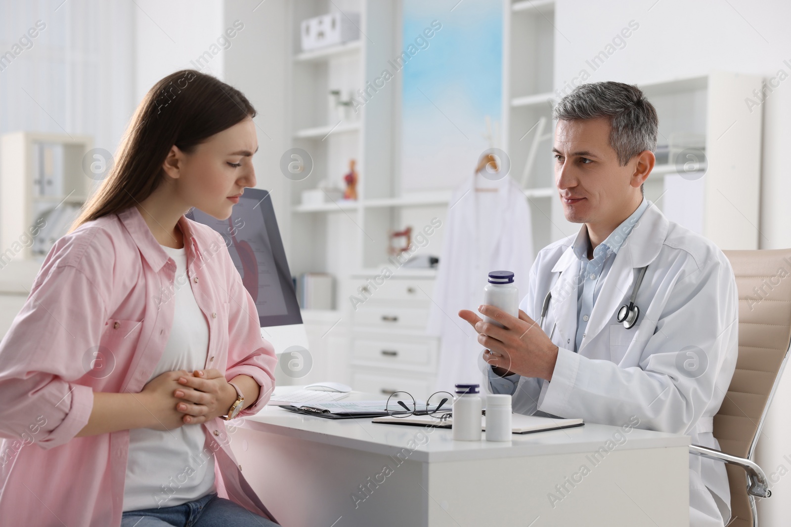 Photo of Gastroenterologist with pills consulting patient at table in clinic
