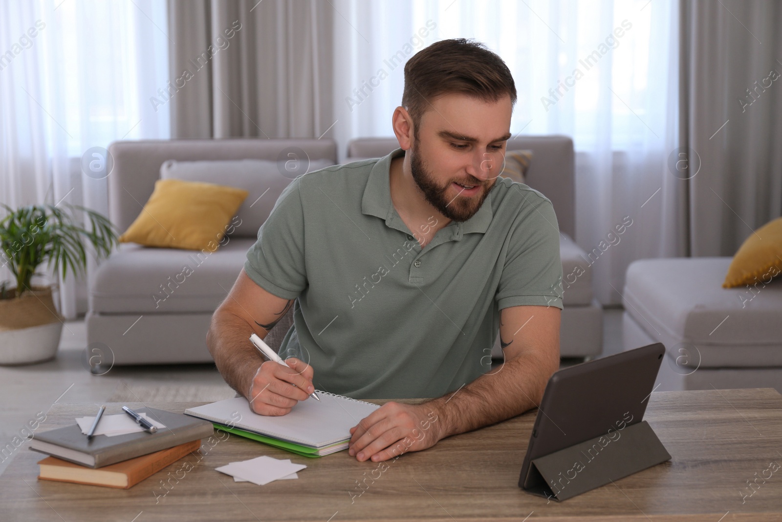 Photo of Young man taking notes during online webinar at table indoors