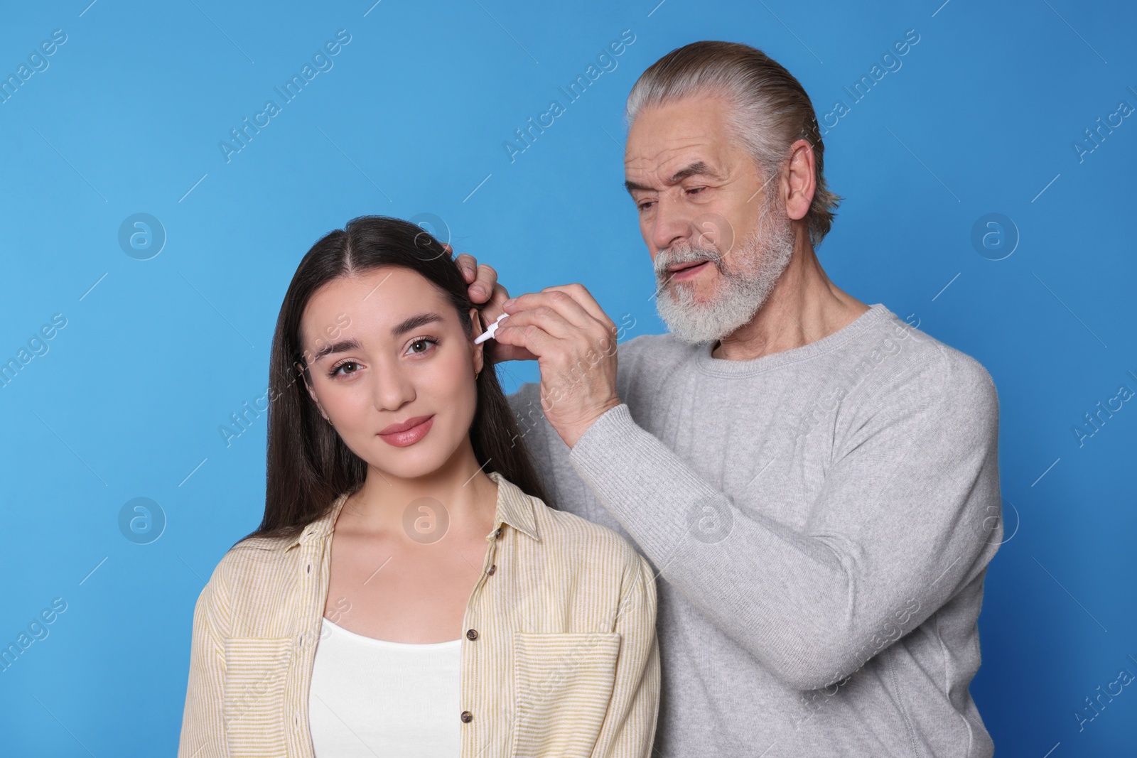 Photo of Senior man dripping medication into woman's ear on light blue background