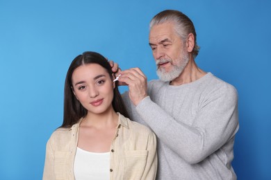 Photo of Senior man dripping medication into woman's ear on light blue background