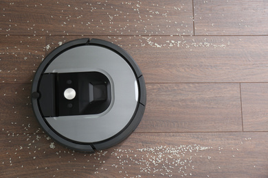 Photo of Modern robotic vacuum cleaner removing scattered rice from wooden floor, top view. Space for text