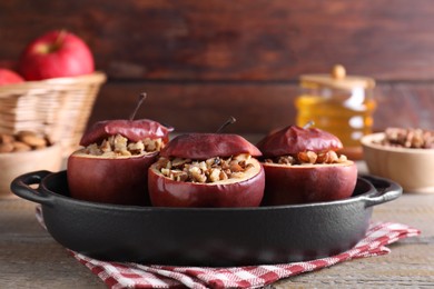 Photo of Tasty baked apples with nuts in baking dish on wooden table, closeup