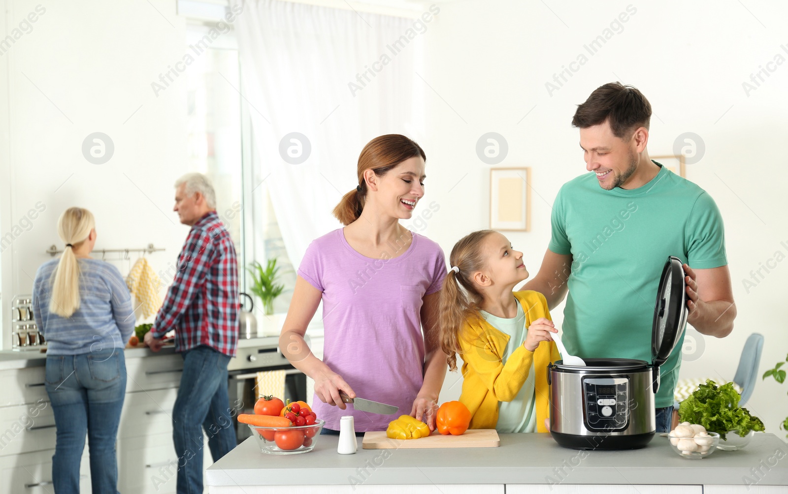 Photo of Happy family preparing food with modern multi cooker in kitchen