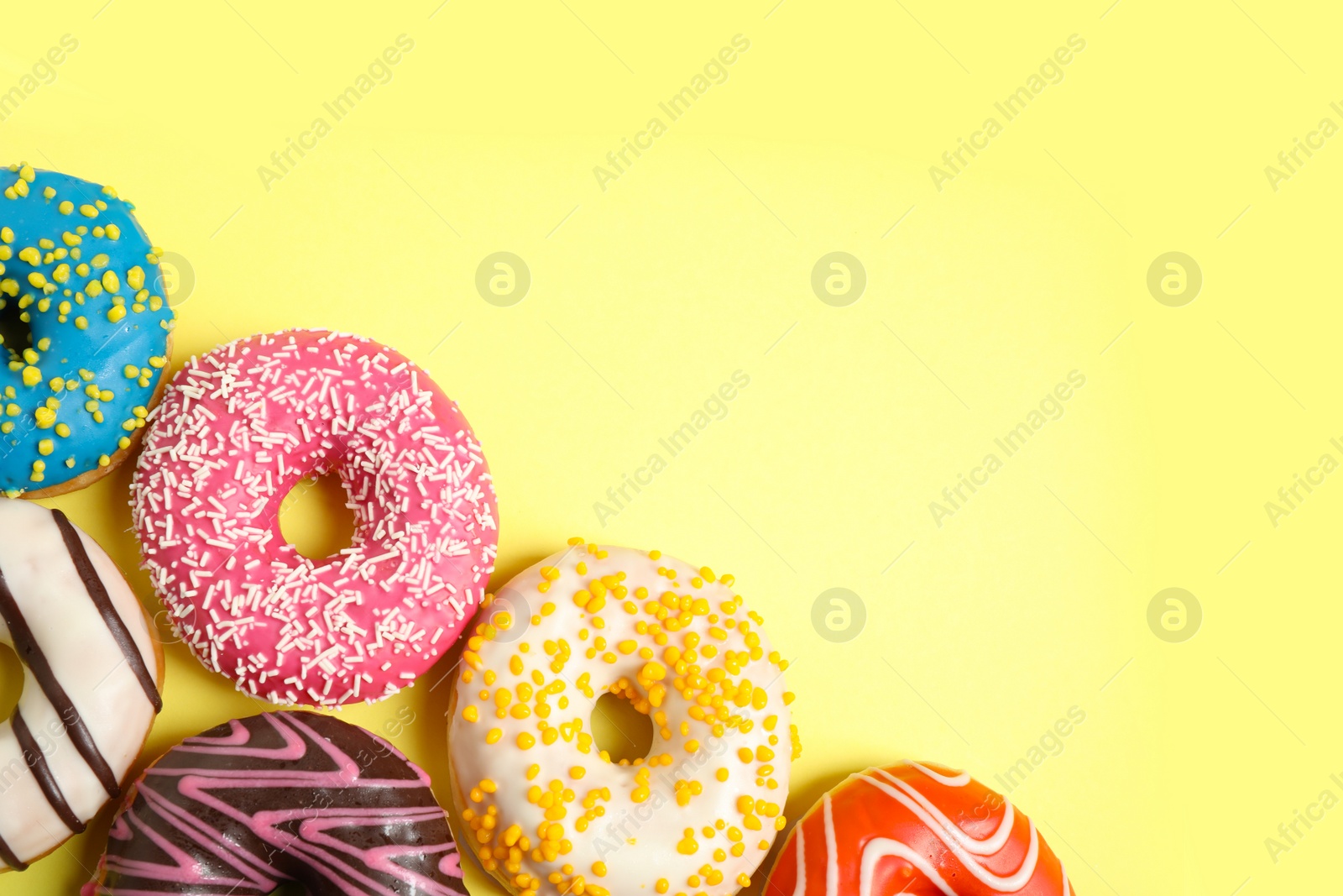 Photo of Delicious glazed donuts on yellow background, flat lay. Space for text