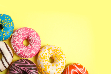 Photo of Delicious glazed donuts on yellow background, flat lay. Space for text