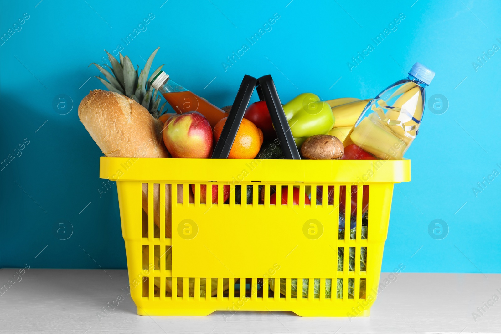 Photo of Shopping basket with grocery products on white table against light blue background