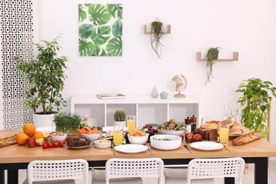 Healthy vegetarian food, glasses of juice, cutlery and plates on wooden table indoors