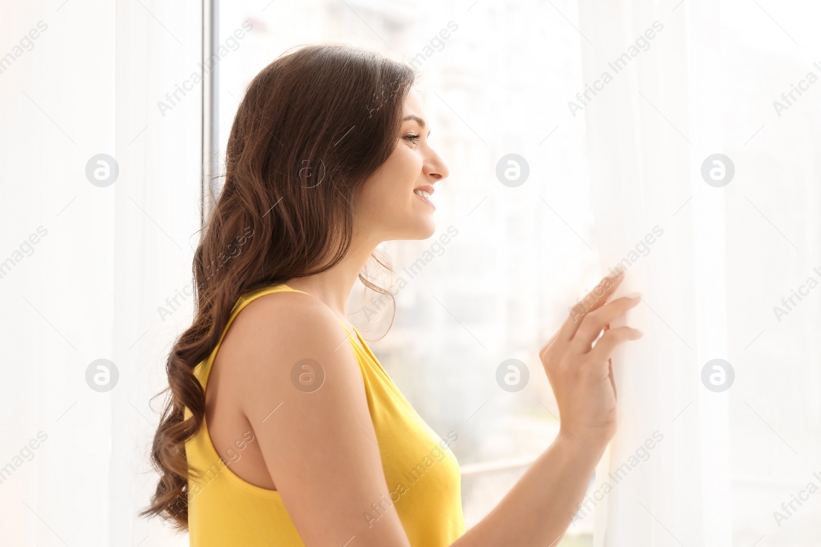 Photo of Beautiful young woman looking out of window at home