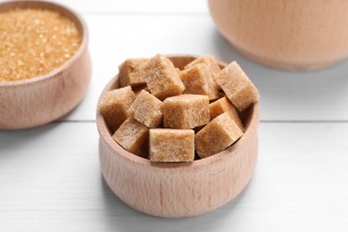 Photo of Different types of brown sugar in bowls on white wooden table, closeup