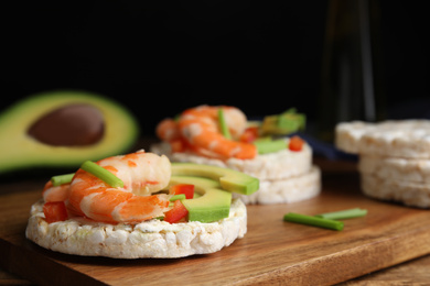 Photo of Puffed rice cakes with shrimps and avocado on wooden board, closeup