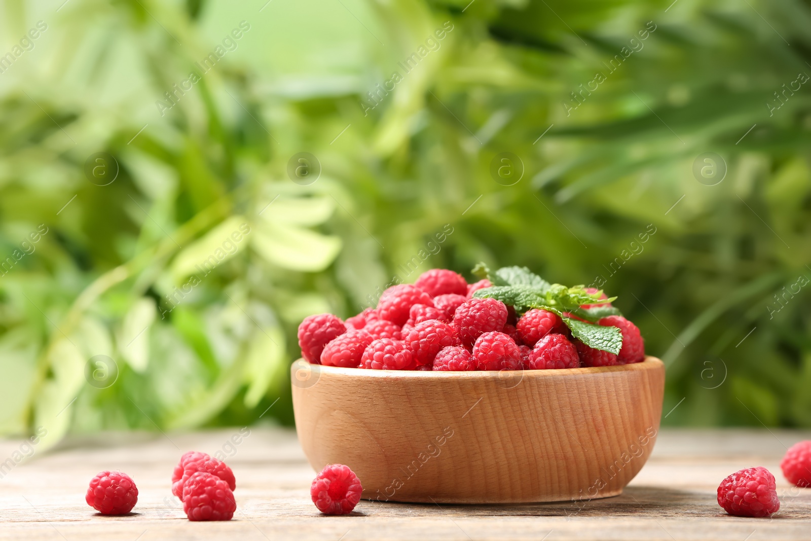 Photo of Bowl with ripe aromatic raspberries on table against blurred background