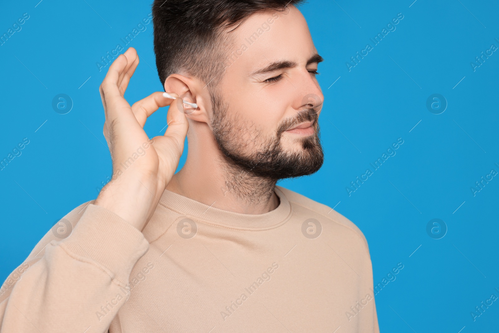 Photo of Young man cleaning ear with cotton swab on light blue background