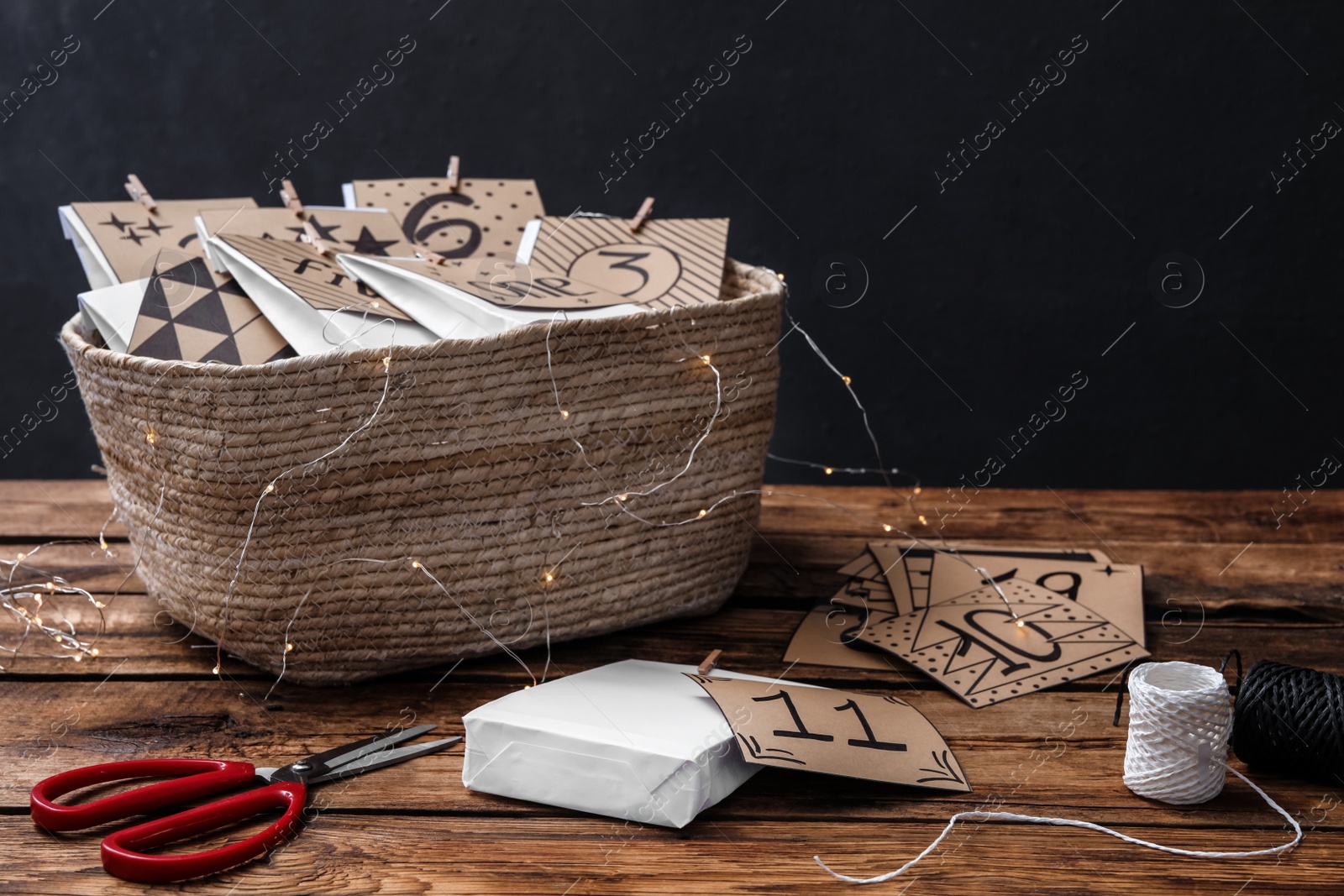 Photo of Many gift bags in wicker basket, scissors and twine on wooden table. Creating advent calendar