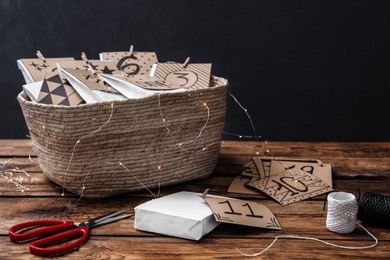 Many gift bags in wicker basket, scissors and twine on wooden table. Creating advent calendar