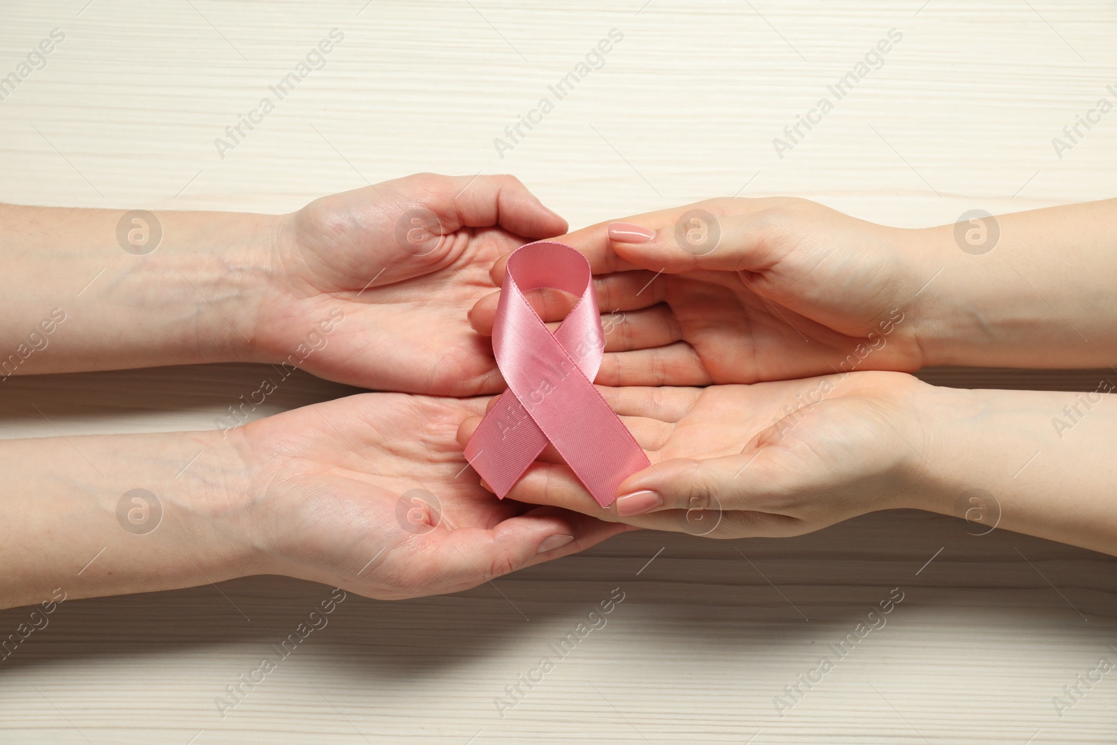 Photo of Women holding pink ribbon at white wooden table, top view. Breast cancer awareness