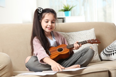 Photo of Cute little girl playing guitar on sofa in room