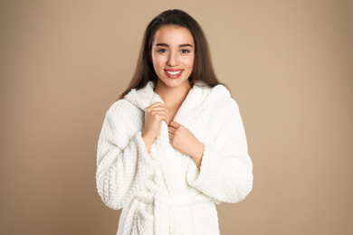 Beautiful young woman in bathrobe on brown background