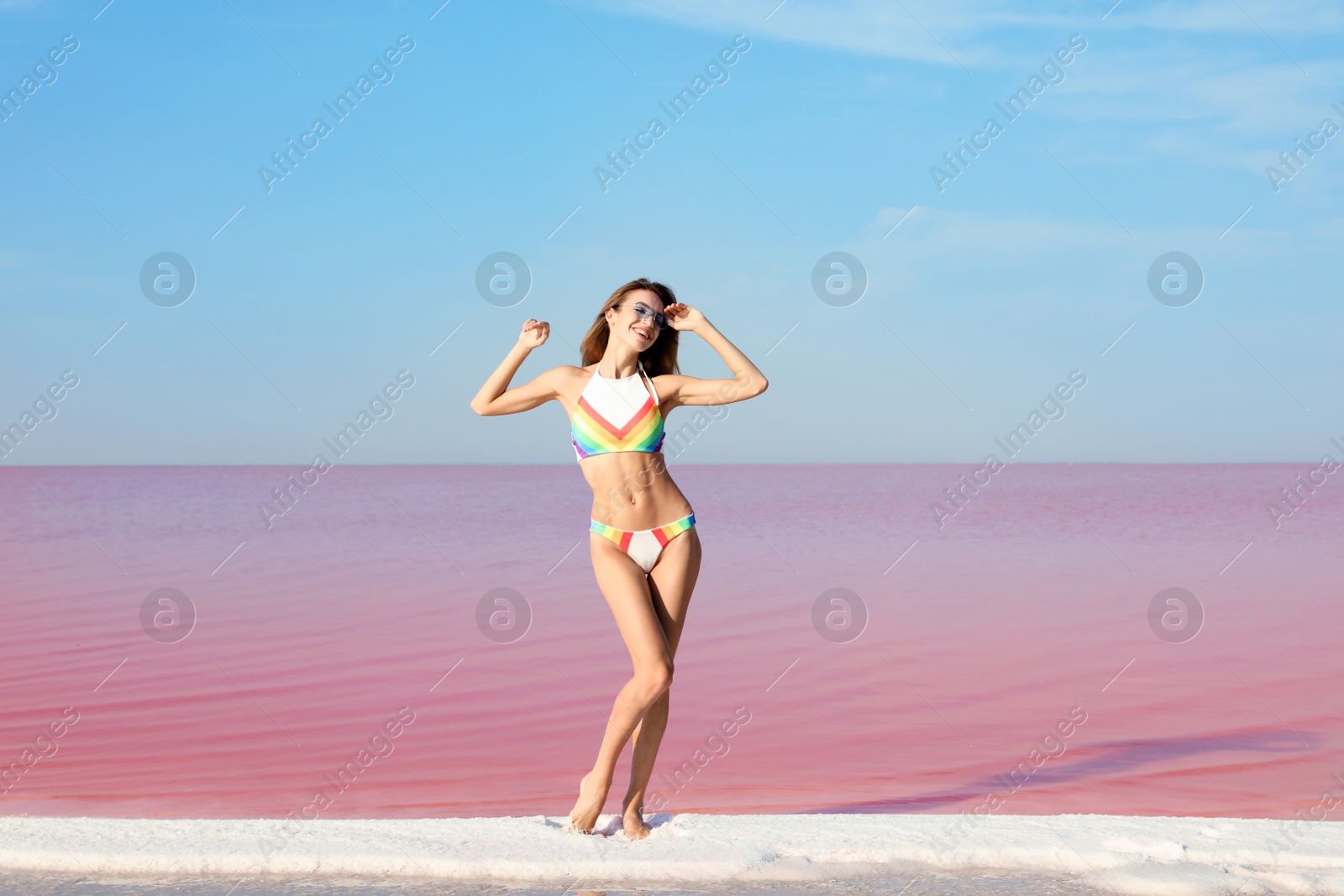 Photo of Beautiful woman in swimsuit standing near pink lake on sunny day