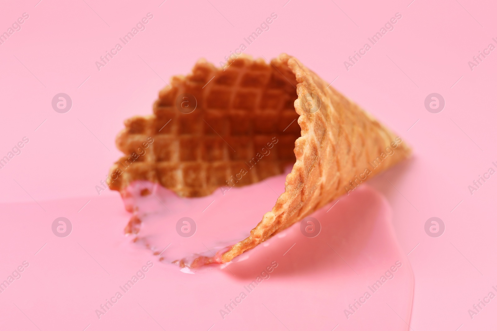 Photo of Melted ice cream and wafer cone on pink background, closeup