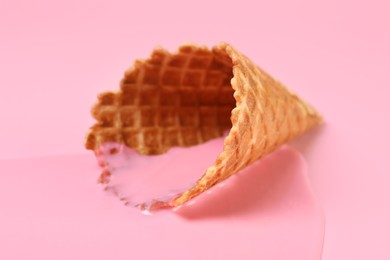 Photo of Melted ice cream and wafer cone on pink background, closeup