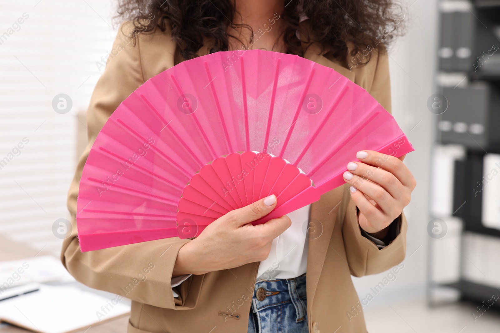 Photo of Woman with pink hand fan in office, closeup