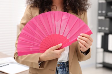 Woman with pink hand fan in office, closeup