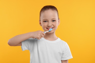 Photo of Happy girl brushing her teeth with toothbrush on yellow background