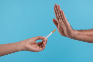 Photo of Stop smoking concept. Man refusing cigarette on light blue background, closeup