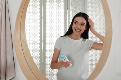 Photo of Woman applying dry shampoo onto her hair near mirror in bathroom