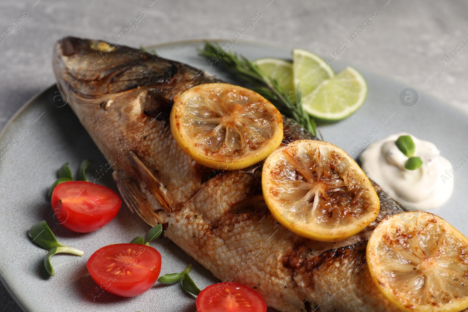 Photo of Delicious baked sea bass fish served with lemon, tomatoes and sauce on table, closeup