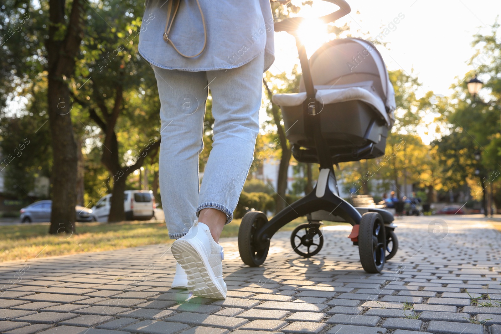 Photo of Young mother walking with her baby in stroller outdoors, closeup