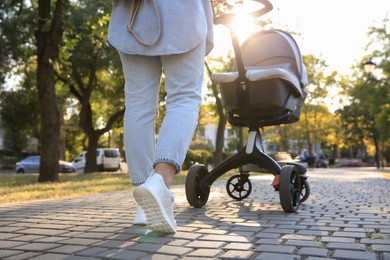 Photo of Young mother walking with her baby in stroller outdoors, closeup