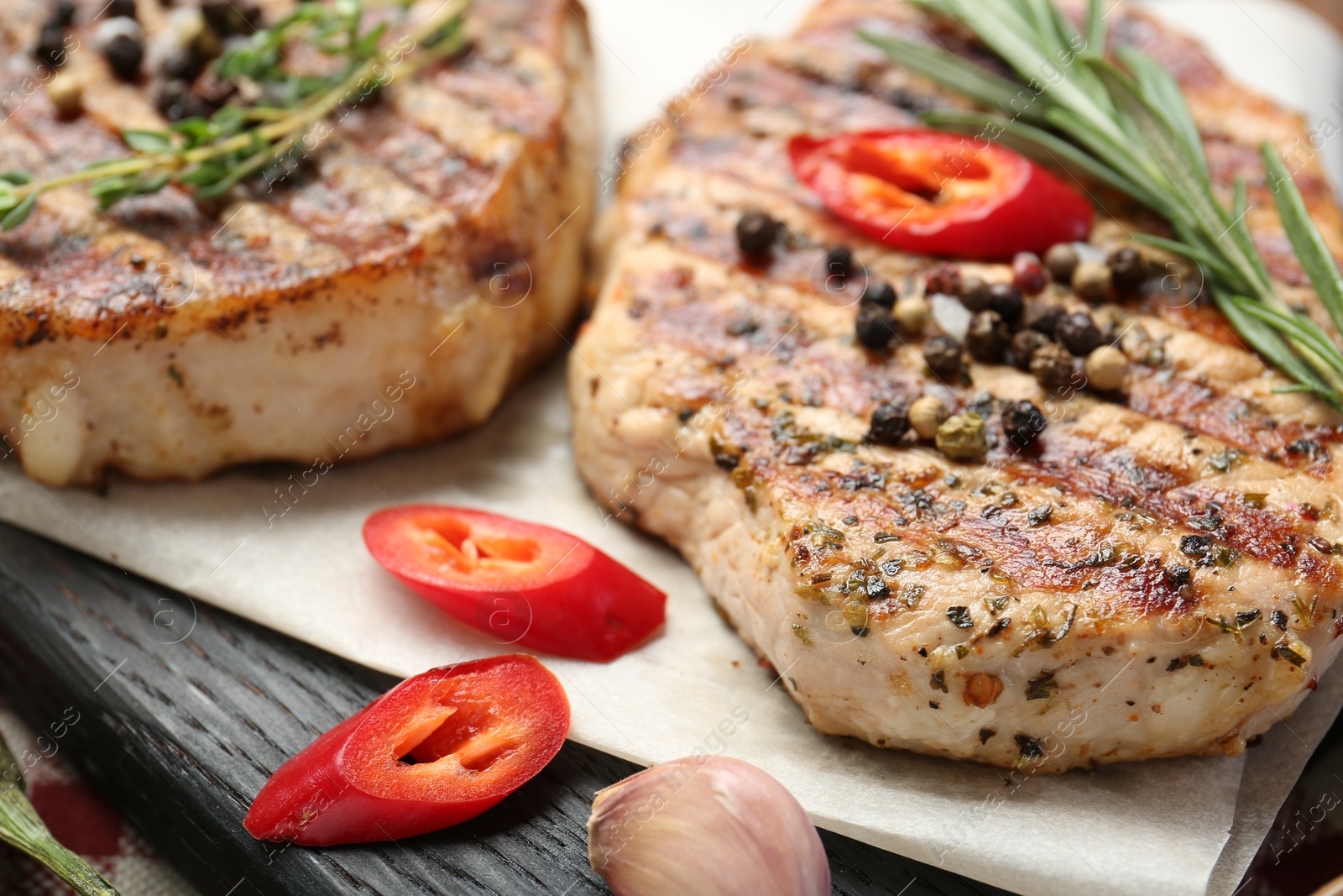 Photo of Delicious grilled pork steaks with spices on board, closeup