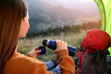 Photo of Young woman with thermos inside of camping tent in mountains