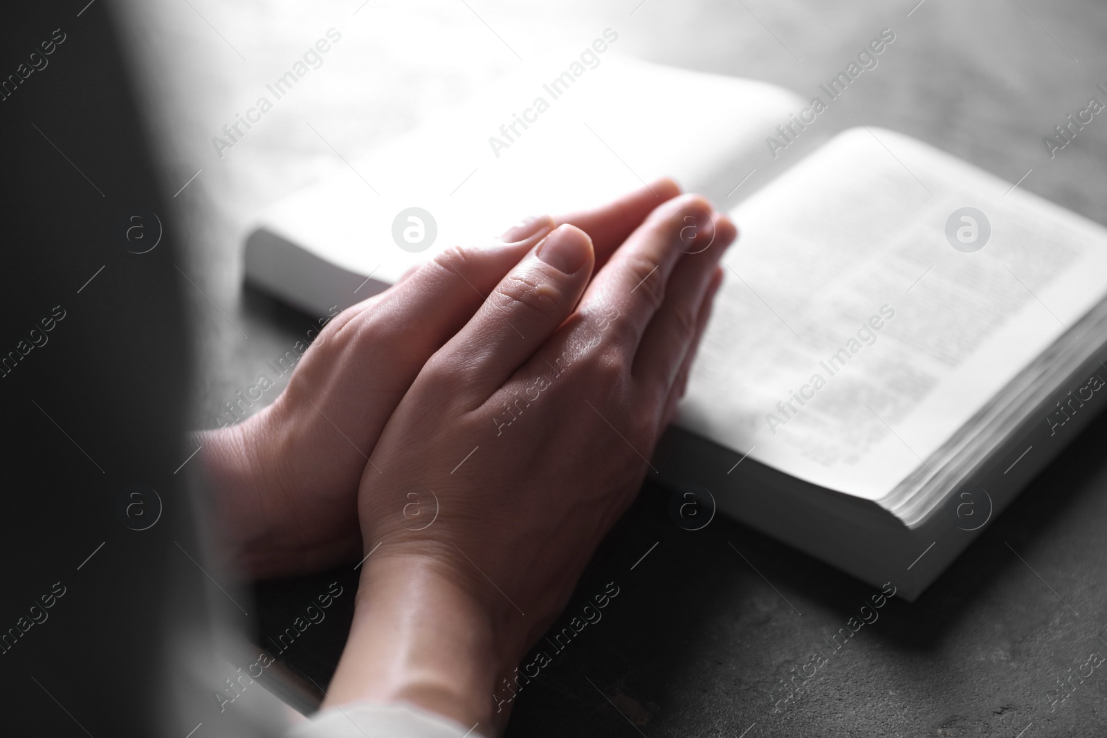 Photo of Religion. Christian woman praying over Bible at gray table, closeup