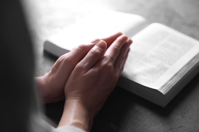 Photo of Religion. Christian woman praying over Bible at gray table, closeup