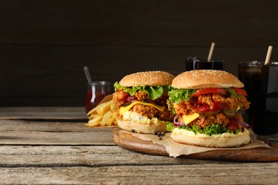 Photo of Delicious burgers with crispy chicken patty, french fries and soda drinks on wooden table. Space for text