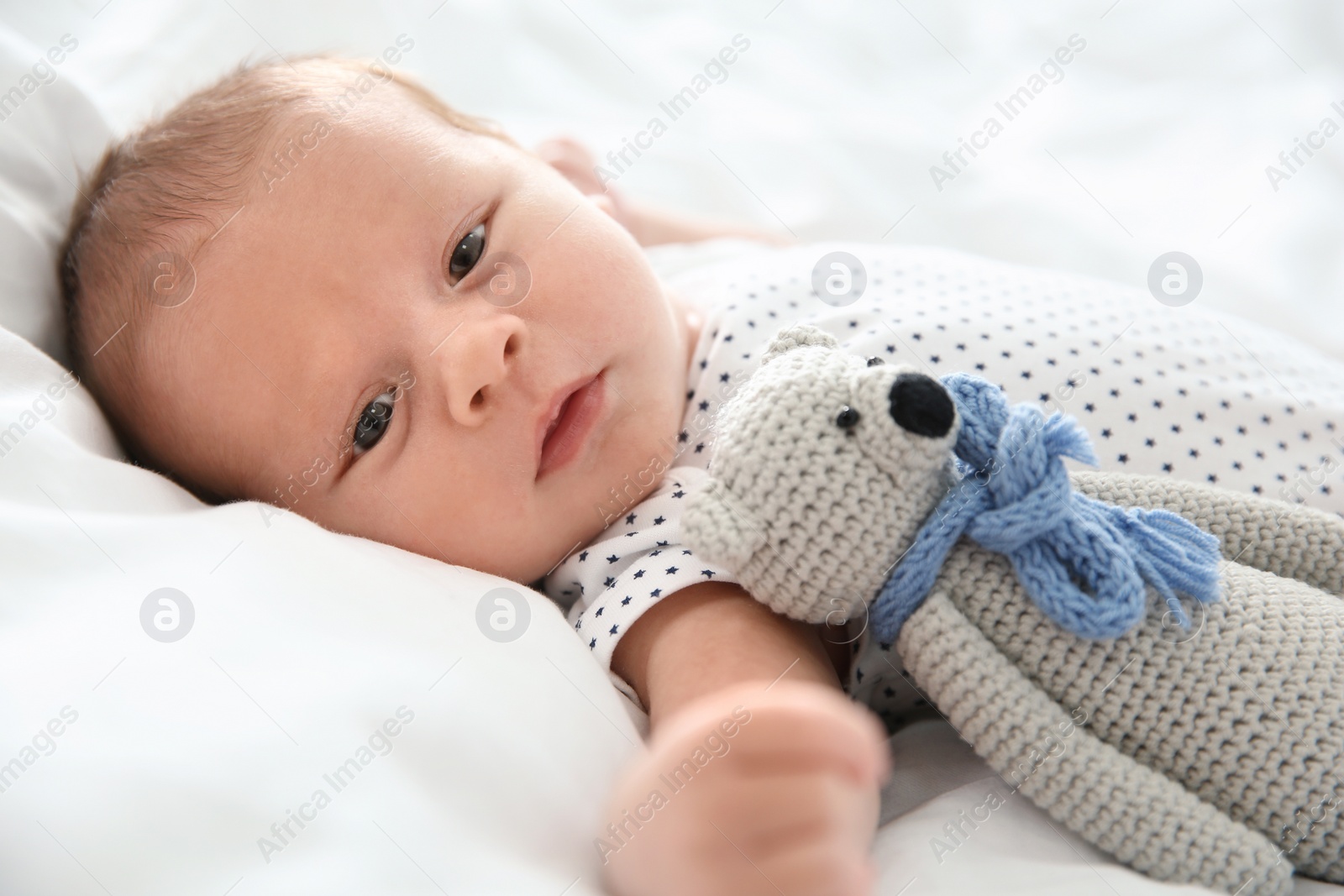 Photo of Adorable newborn baby with toy lying on bed sheet