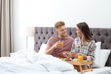 Photo of Happy young couple having romantic breakfast in bed at home
