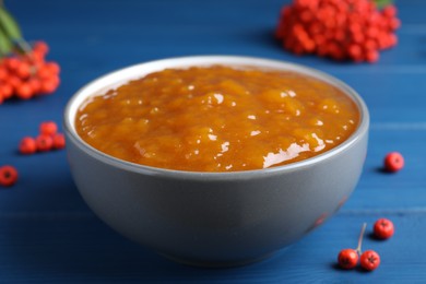 Photo of Delicious rowan jam in ceramic bowl on blue wooden  table, closeup