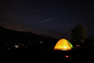 Image of Beautiful view of mountain landscape with glowing camping tent at night