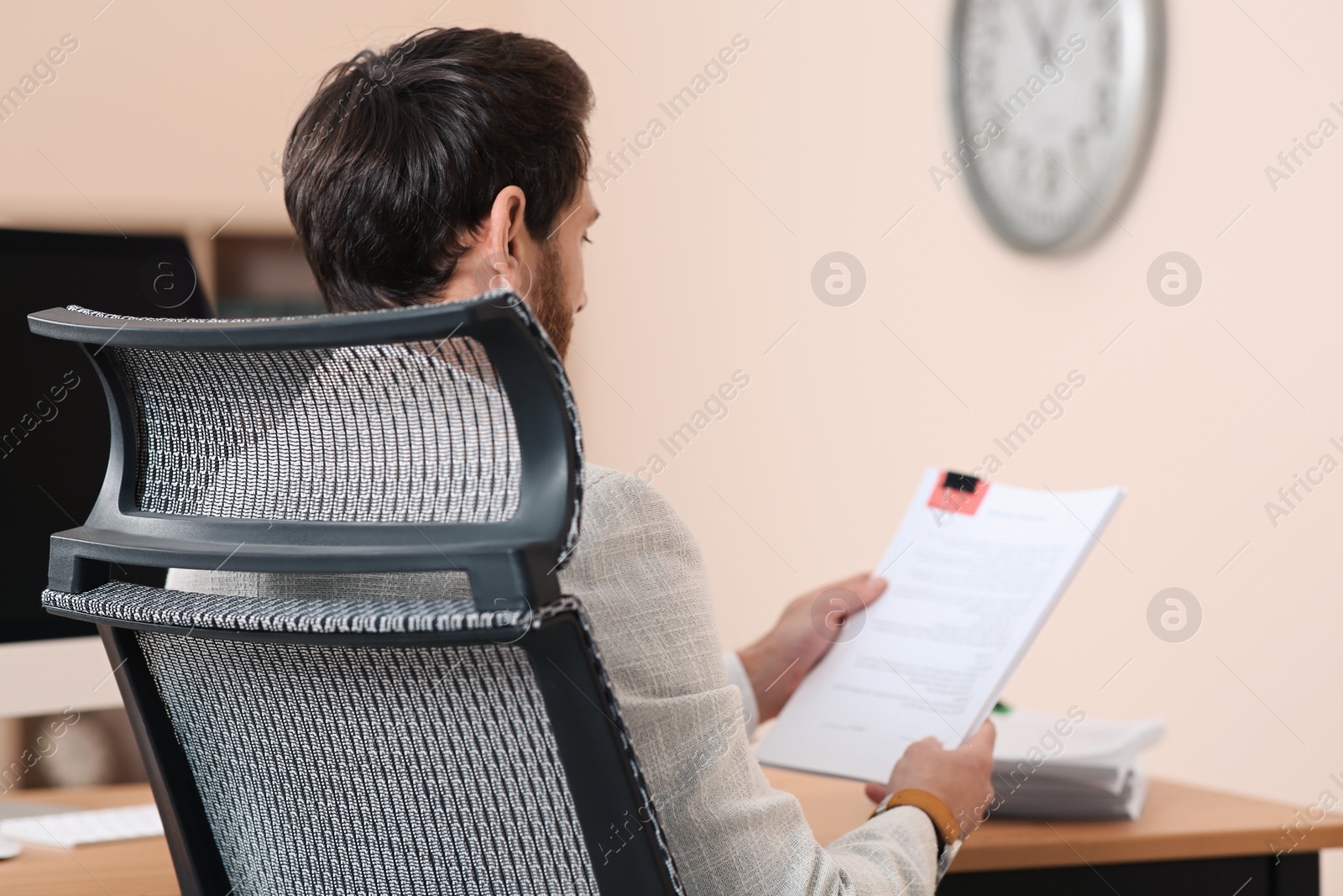 Photo of Man working with documents at wooden table in office, back view