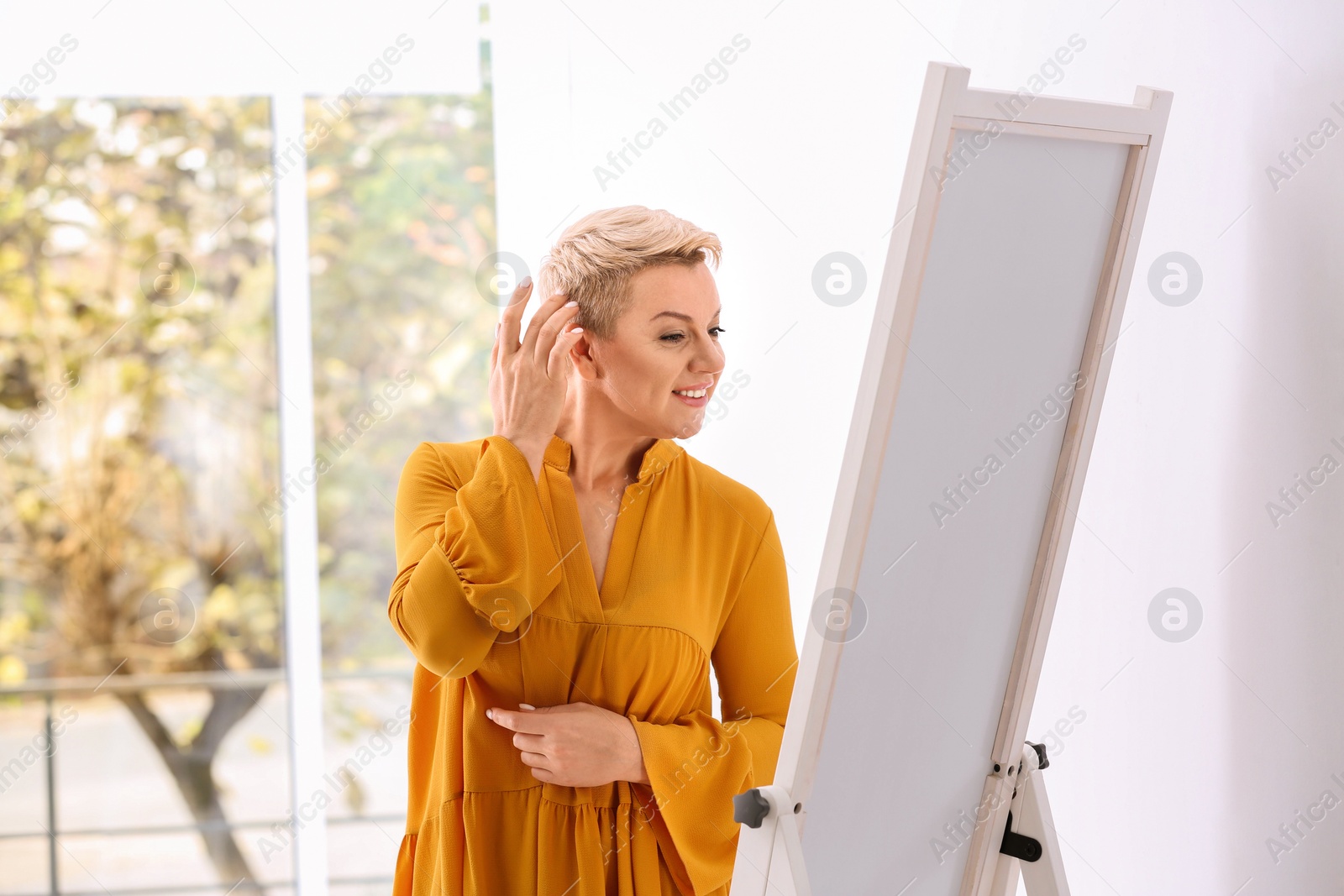 Photo of Beautiful mature woman looking at herself in large mirror indoors