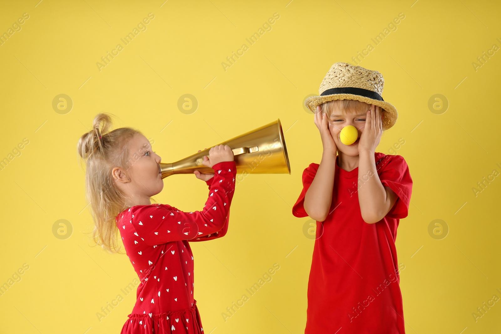 Photo of Funny kids with megaphone on yellow background. April fool's day