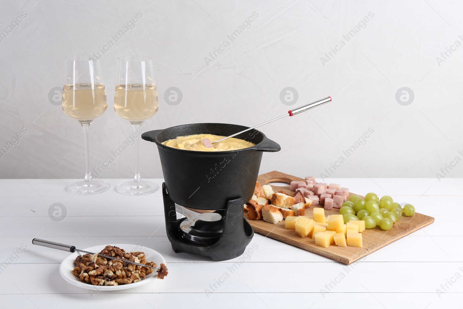 Photo of Fondue pot with tasty melted cheese, forks, wine and different snacks on white wooden table