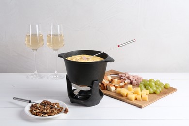 Fondue pot with tasty melted cheese, forks, wine and different snacks on white wooden table